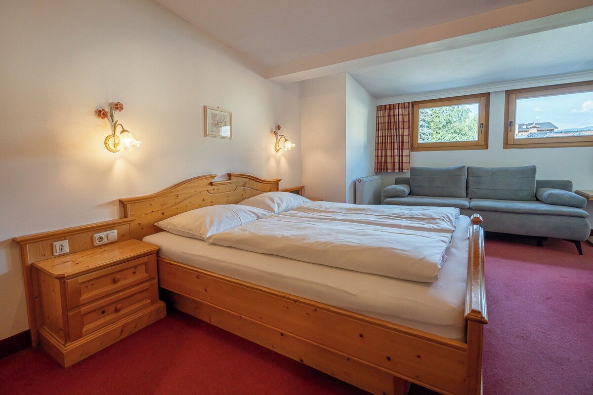 Una camera da letto con un letto di legno, comodini, un divano grigio e una finestra con tende.
