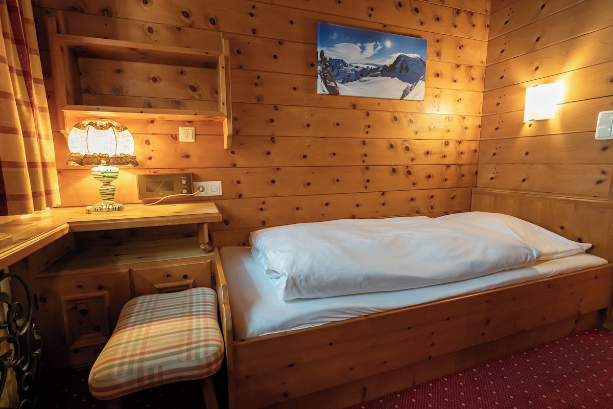 Una camera in legno con un letto, una scrivania, una sedia e una lampada a parete.