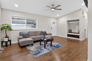 A living room with a gray sectional sofa, a coffee table, a ceiling fan, a window with blinds, and a built-in closet. - Beautiful Bungalow near Buckhead (Doraville)