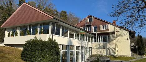 A modern two-story house with a large glass facade, a red roof, and a stone pathway leading to the entrance.