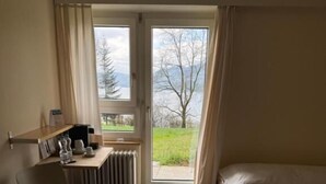 A hotel room with a bed, a chair, a desk with a computer, and a window with a view of trees and mountains.