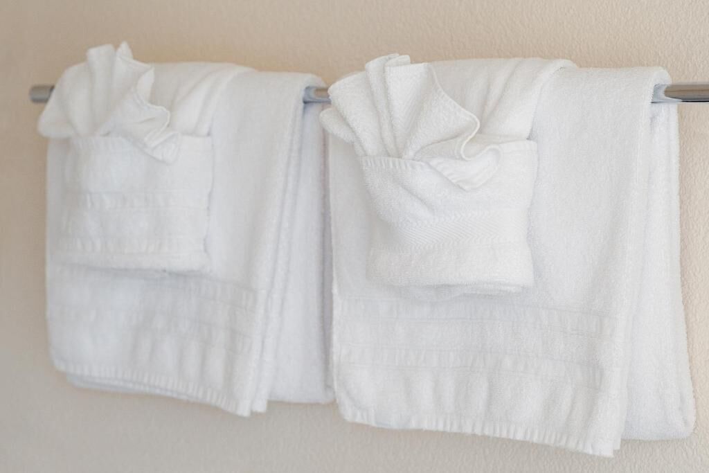Two white towels hanging on a metal towel rack against a plain wall.
