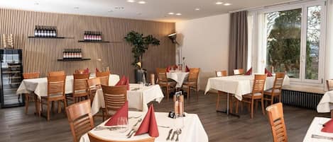 A restaurant with multiple tables, chairs, and a wooden wall with wine bottles.