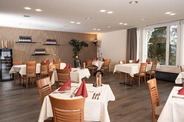 A restaurant with multiple tables, chairs, and a wooden wall with wine bottles. - Vitabella Rügel (Seengen)