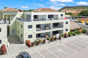 Ein mehrstöckiges Hotel mit Balkonen, einem Parkplatz und einem Gebäude mit Strohdeckung im Hintergrund.