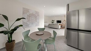 Et moderne køkken med et stålkøleskab, et spiseområde med et rundt bord og stole, samt en opholdsstue med sofa og tv.