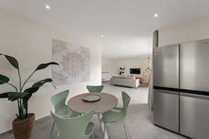 Eine moderne Küche mit einem Edelstahlkühlschrank, ein Essbereich mit rundem Tisch und Stühlen sowie ein Wohnbereich mit Sofa und Fernseher.