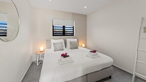 A modern bedroom with a large bed, bedside lamps, a window with a view, and a white wall.