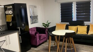 A modern kitchen with a black refrigerator, a purple sofa, a dining table with wooden legs, and a window with blinds. - Private Movie Theater in Calais • XXL Screen • Immersive sound (Calais)