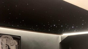 A bedroom with a starry ceiling, a bed with a grey mattress, a small table with a 'Movie Night' sign, and a framed picture on the wall. - Private Movie Theater in Calais • XXL Screen • Immersive sound (Calais)