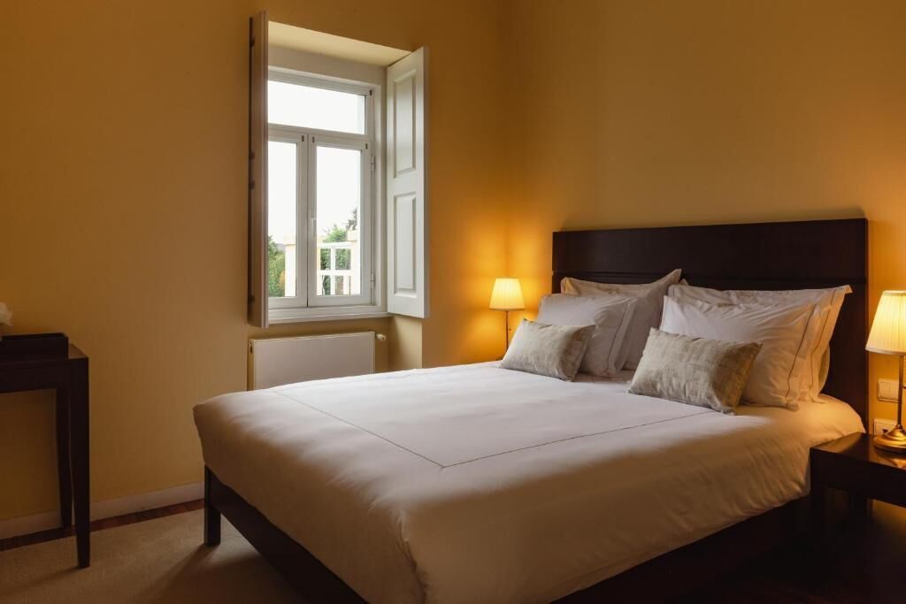 A hotel room with a bed, bedside lamps, a window, and a nightstand.