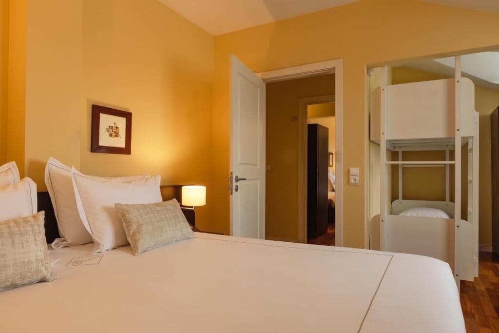 Una habitación de hotel con cama, mesita de noche, lámpara y una puerta que da a un baño.