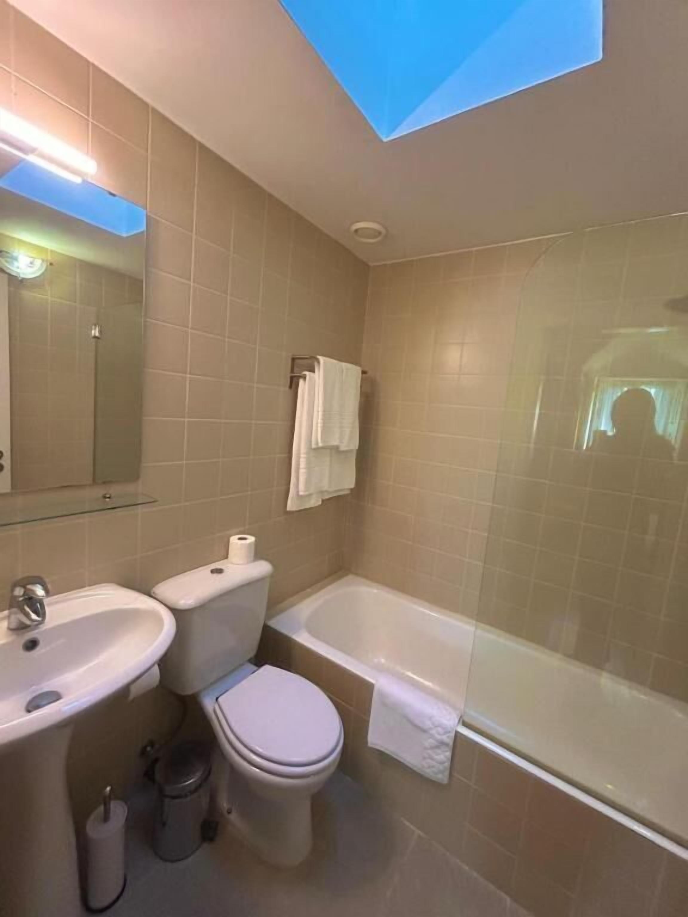 Un baño con tragaluz, bañera, inodoro y lavamanos.