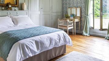 Un dormitorio con cama, mesita de noche, cómoda, silla y ventana con cortinas.