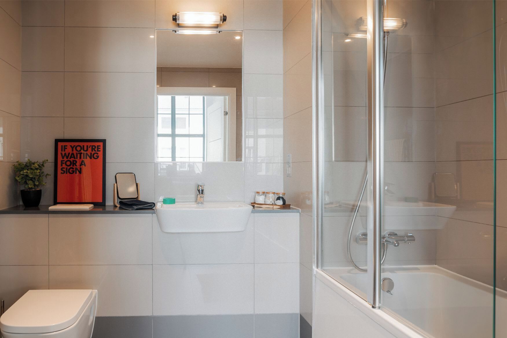Ein modernes Badezimmer mit Duschkabine aus Glas, einem Waschbecken mit Spiegel darüber und einer Toilette.