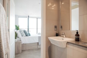Ein modernes Badezimmer mit einem weißen Waschbecken, einem großen Spiegel und einer Shampoo-Flasche.