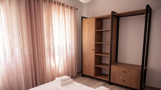 Een slaapkamer met een bed, een houten kledingkast en dunne gordijnen.