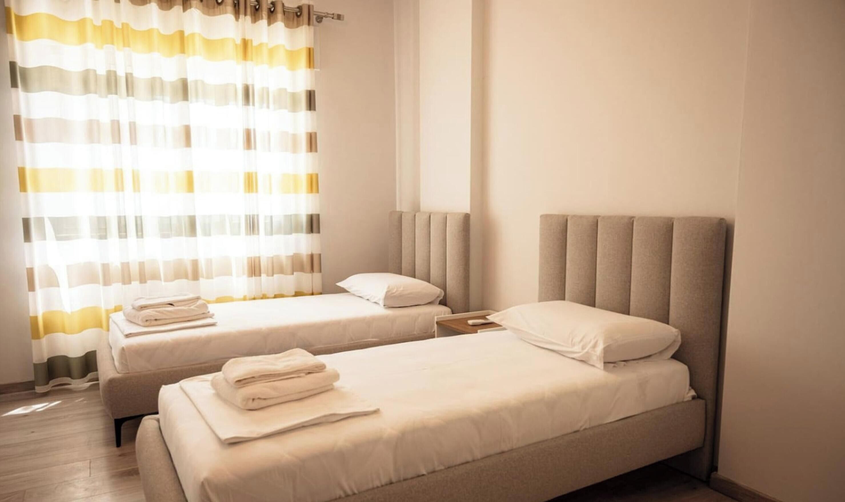 A hotel room with two beds, a large window with curtains, and a neutral color scheme.