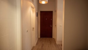 Een smalle gang met een houten vloer, witte wanden en een houten deur aan het einde.