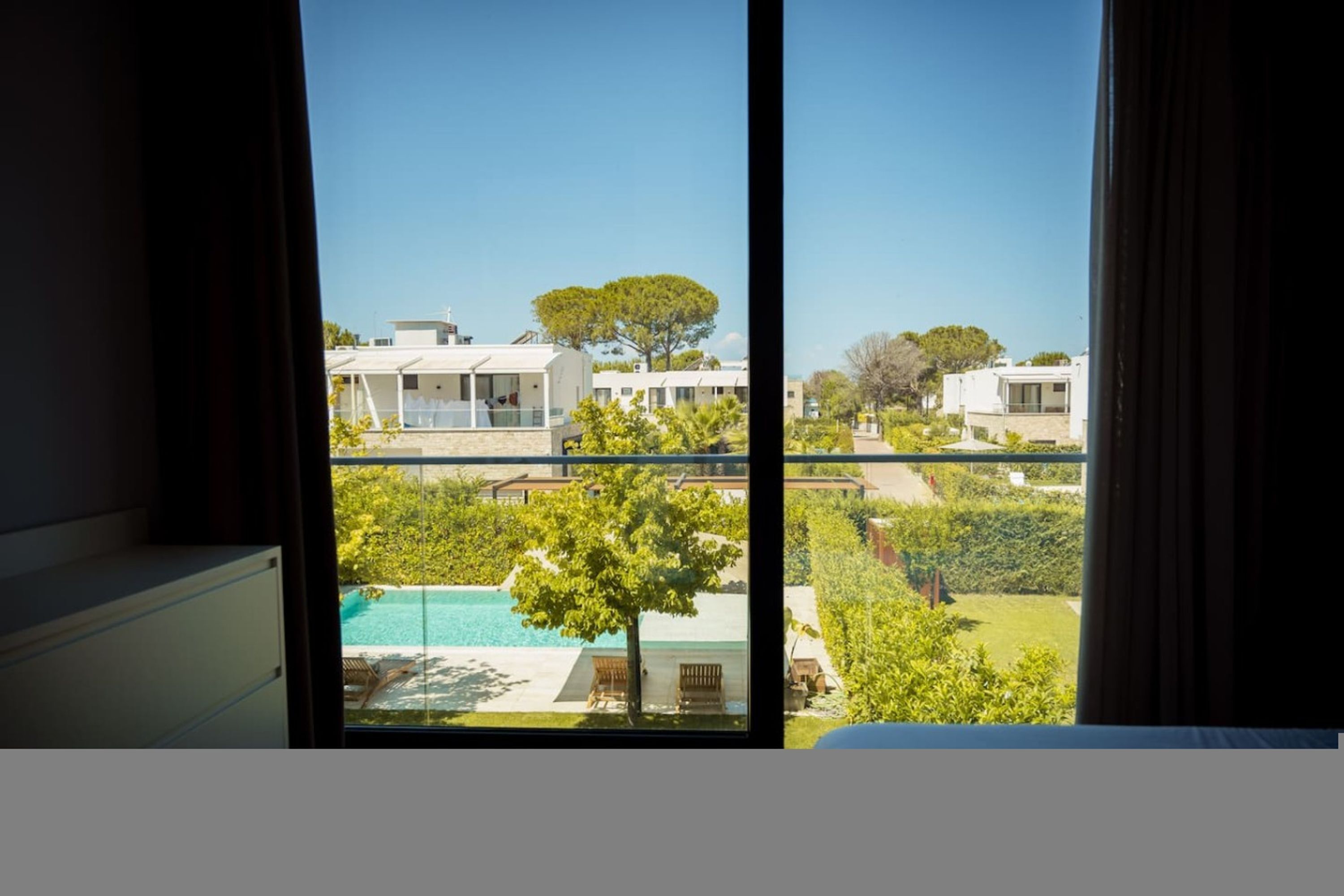 A view from a window of a modern building with a pool, greenery, and other structures in the background.