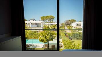 A view from a window of a modern building with a pool, greenery, and other structures in the background.