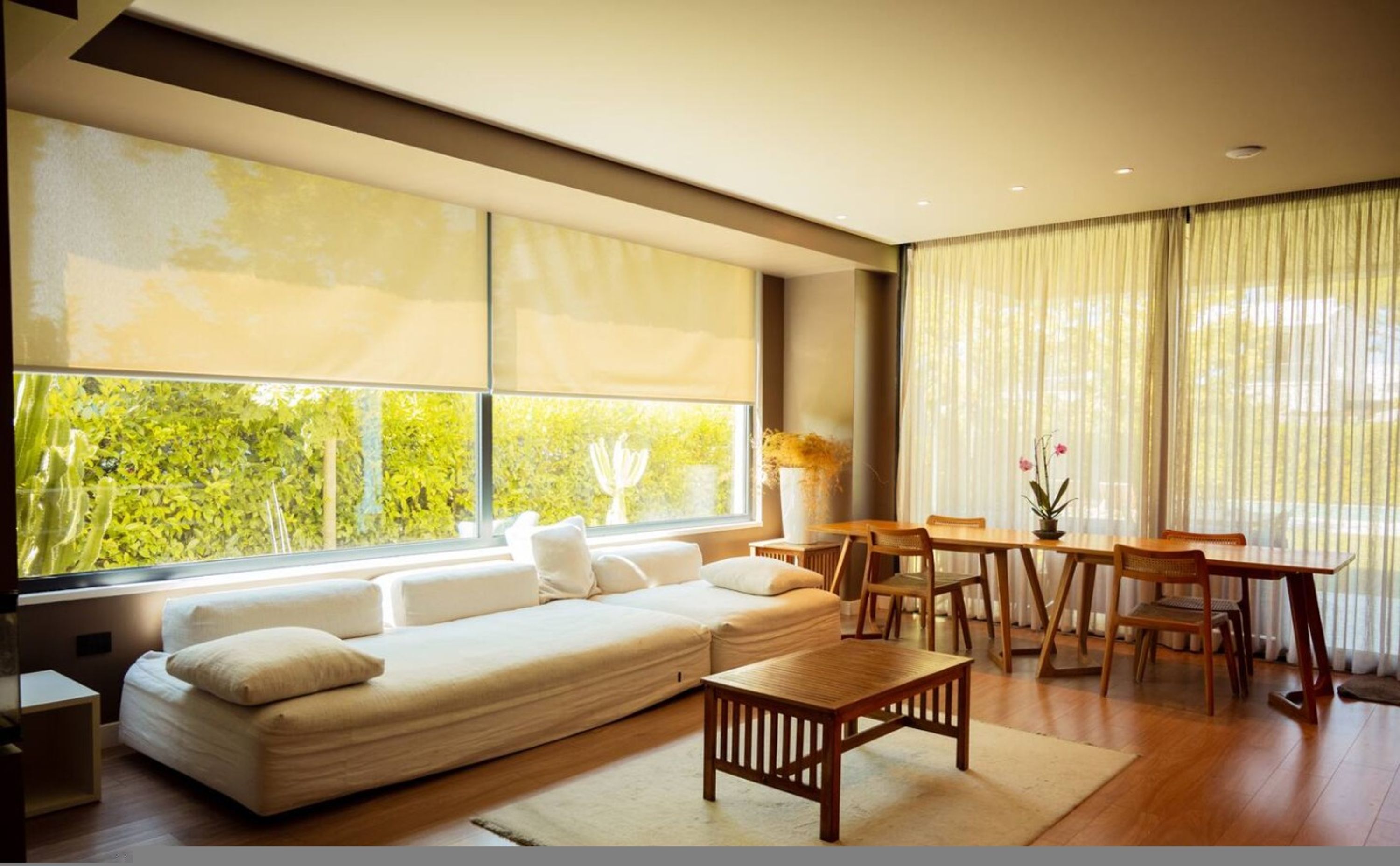 A modern living room with a large window, a sofa, a dining table, and chairs.
