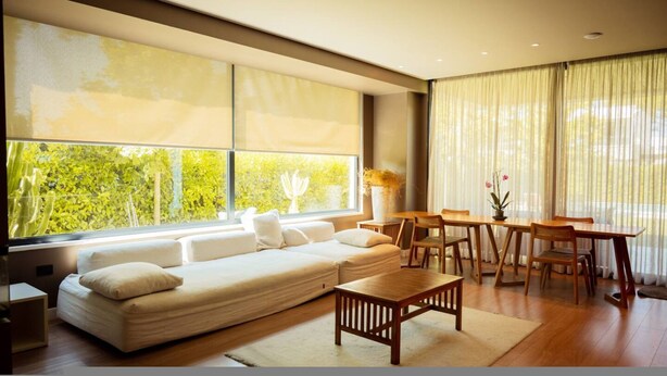 A modern living room with a large window, a sofa, a dining table, and chairs. - Villa with Pool | San Pietro Resort (Durrës)