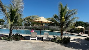 Ein Poolbereich mit Liegestühlen, Palmen und wolkenlosem, blauem Himmel.