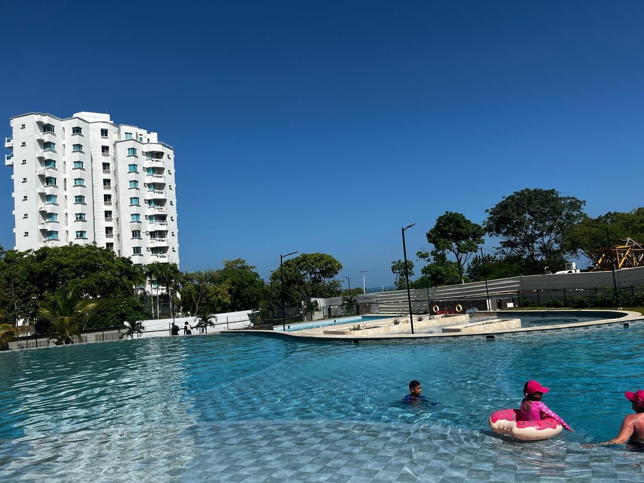 A swimming pool with clear blue water, surrounded by a white building and trees.