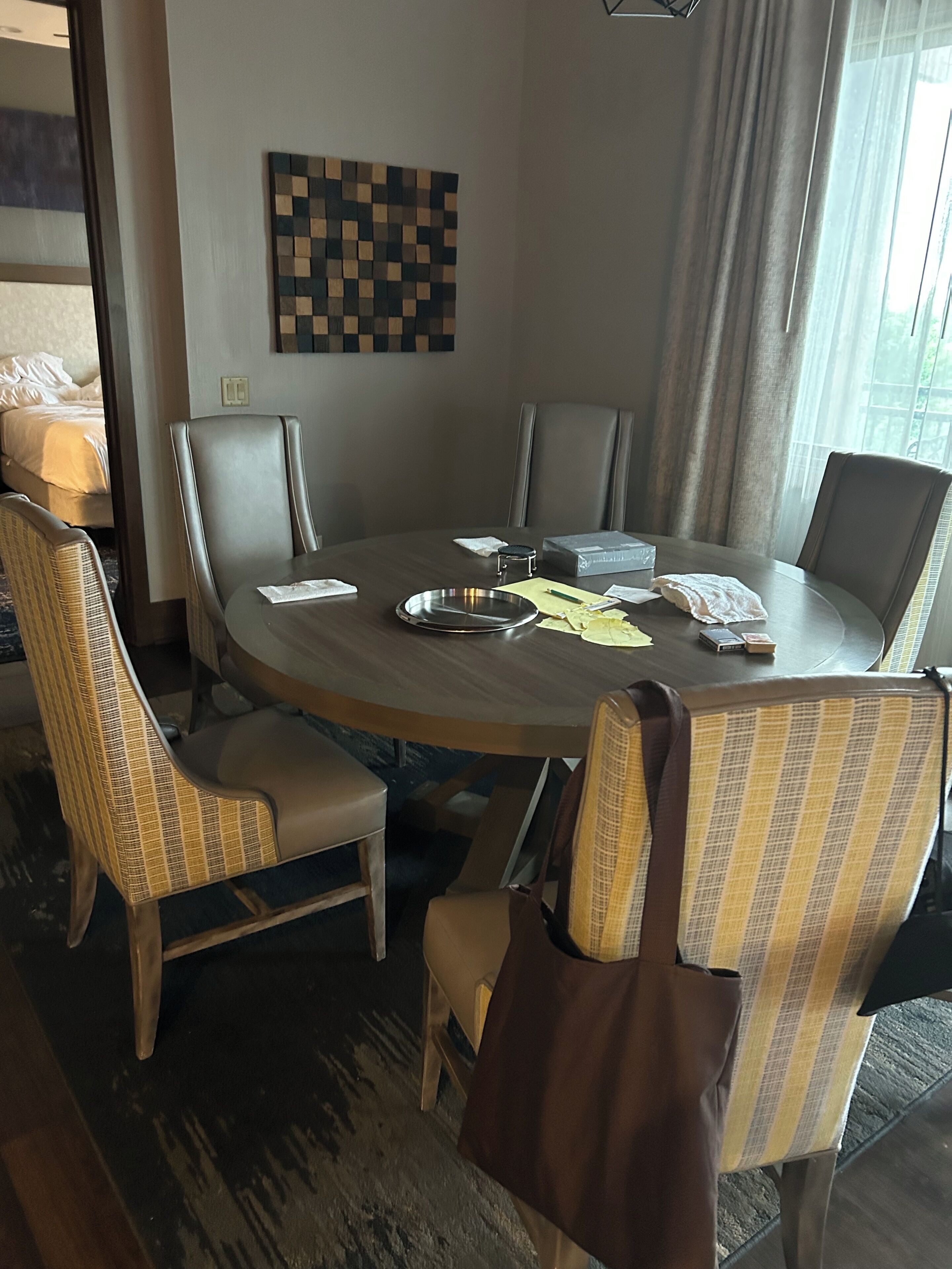 Une chambre d’hôtel avec une table de salle à manger ronde, quatre chaises, un lit et une fenêtre avec des rideaux.