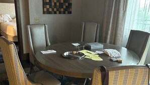Ett hotellrum med ett runt matbord, fyra stolar, en säng och ett fönster med gardiner.