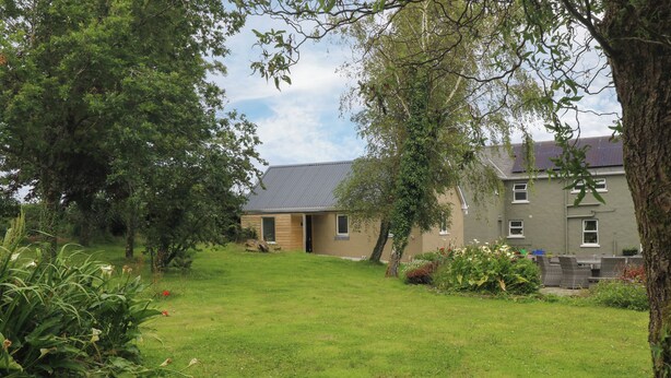 A residential property with a grassy yard, a wooden door, and a grey building with multiple windows. - Mayfly Cottage (Clonbur)
