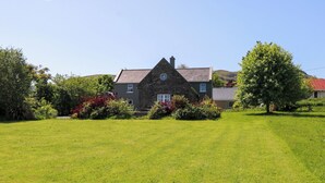 A house with a stone facade, a well-maintained lawn, and a large tree in the foreground. - Mayfly Cottage (Clonbur)