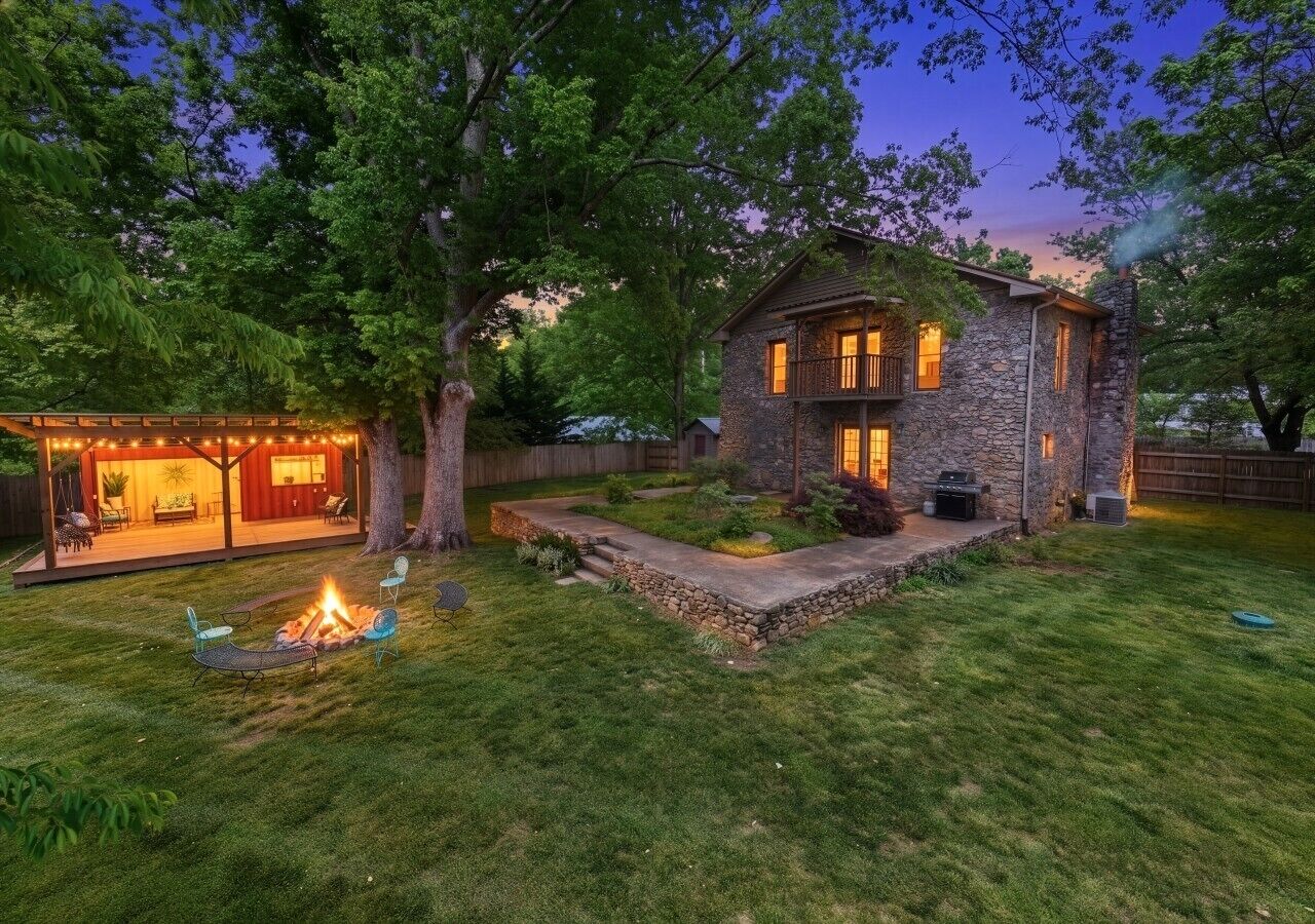 A stone house with a fire pit and outdoor seating, surrounded by a well-maintained lawn and trees.