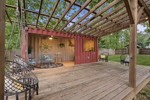 A wooden deck with a covered seating area, a compass wall decoration, and outdoor furniture. - Eclectic Asheville Escape w Fire Pit & Yard! (Asheville)
