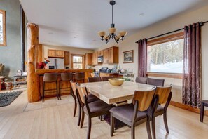 A modern kitchen with wooden cabinets, a central island, and a dining area with a large table and chairs. - 400 Whispering Pines Dr. (Blue River)