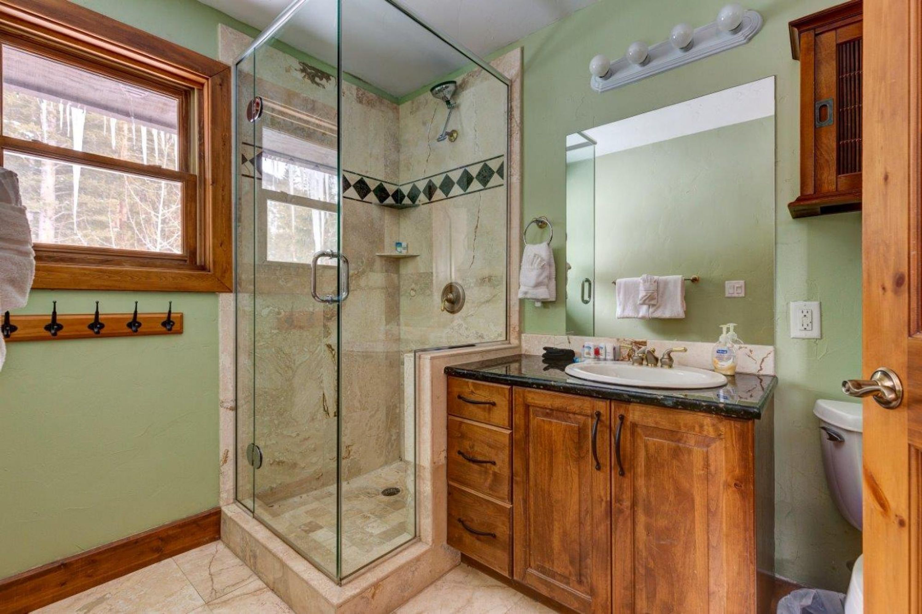 Un bagno con box doccia in vetro, mobili contenitori in legno, un lavandino e un water.