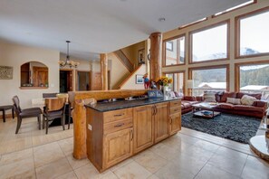 A spacious living area with a wooden island, a staircase, and large windows offering mountain views. - 400 Whispering Pines Dr. (Blue River)