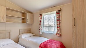 A bedroom with two beds, wooden cabinets, and a window with patterned curtains.