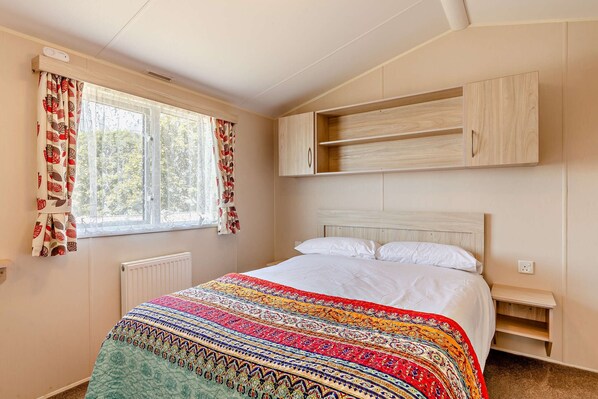 Une chambre à coucher avec un lit, une fenêtre avec des rideaux, un radiateur et une armoire en bois placée au-dessus du lit.