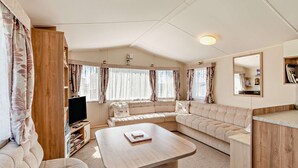 A cozy RV interior with a sofa, a small table, a TV, and a mirror.