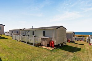Une maison mobile avec une cour clôturée, un petit abri de jardin et deux réservoirs de propane.