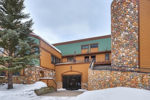 A building with a stone facade, a green roof, and a snow-covered ground. - Sundowner II 203 in Breckenridge (Breckenridge)
