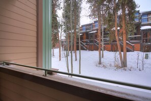 A view from a window with a metal railing, overlooking a building with multiple balconies and a snowy ground. - Sundowner II 203 in Breckenridge (Breckenridge)