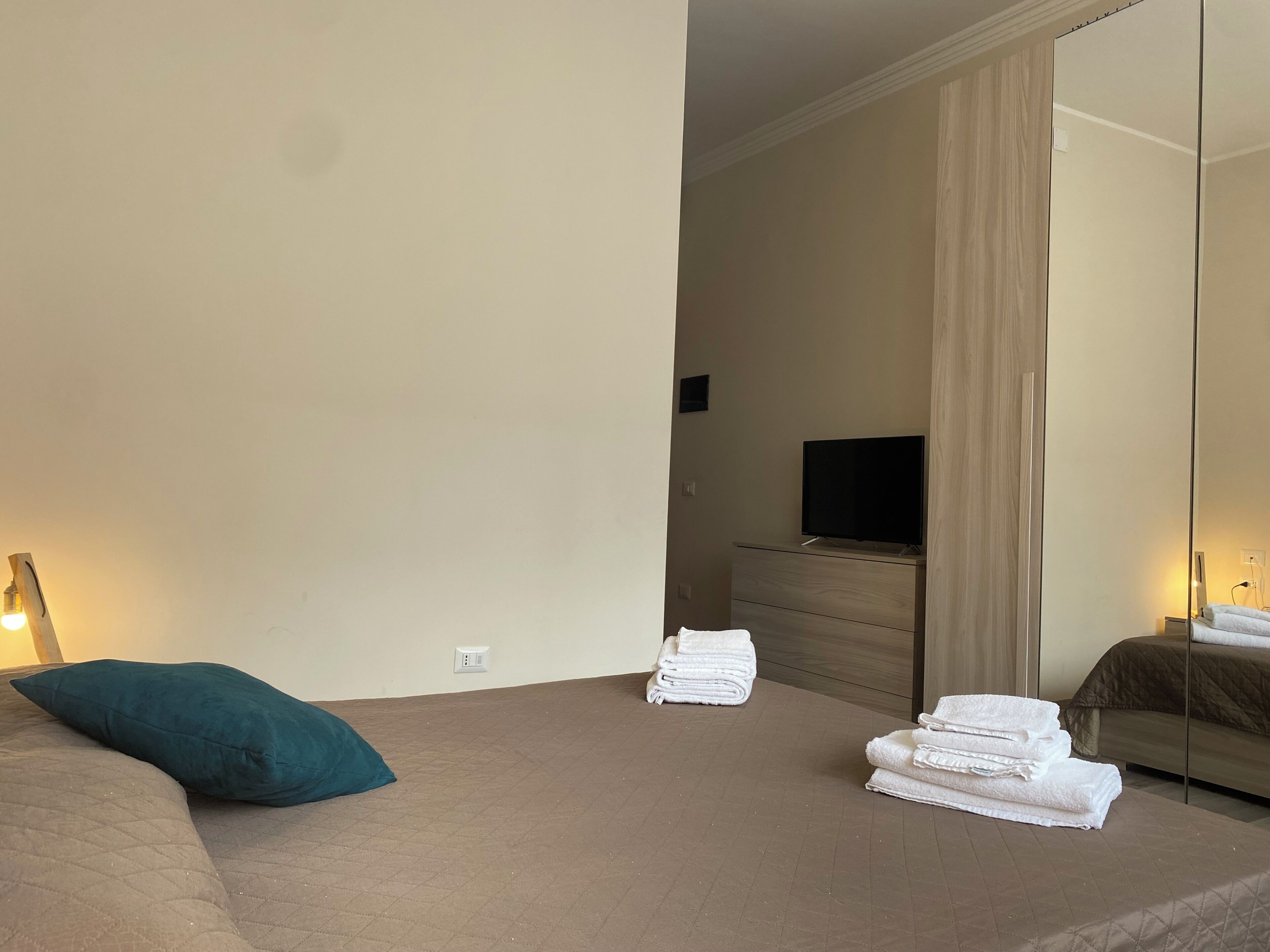 A bedroom with a bed, a dresser, a TV, and a mirror.