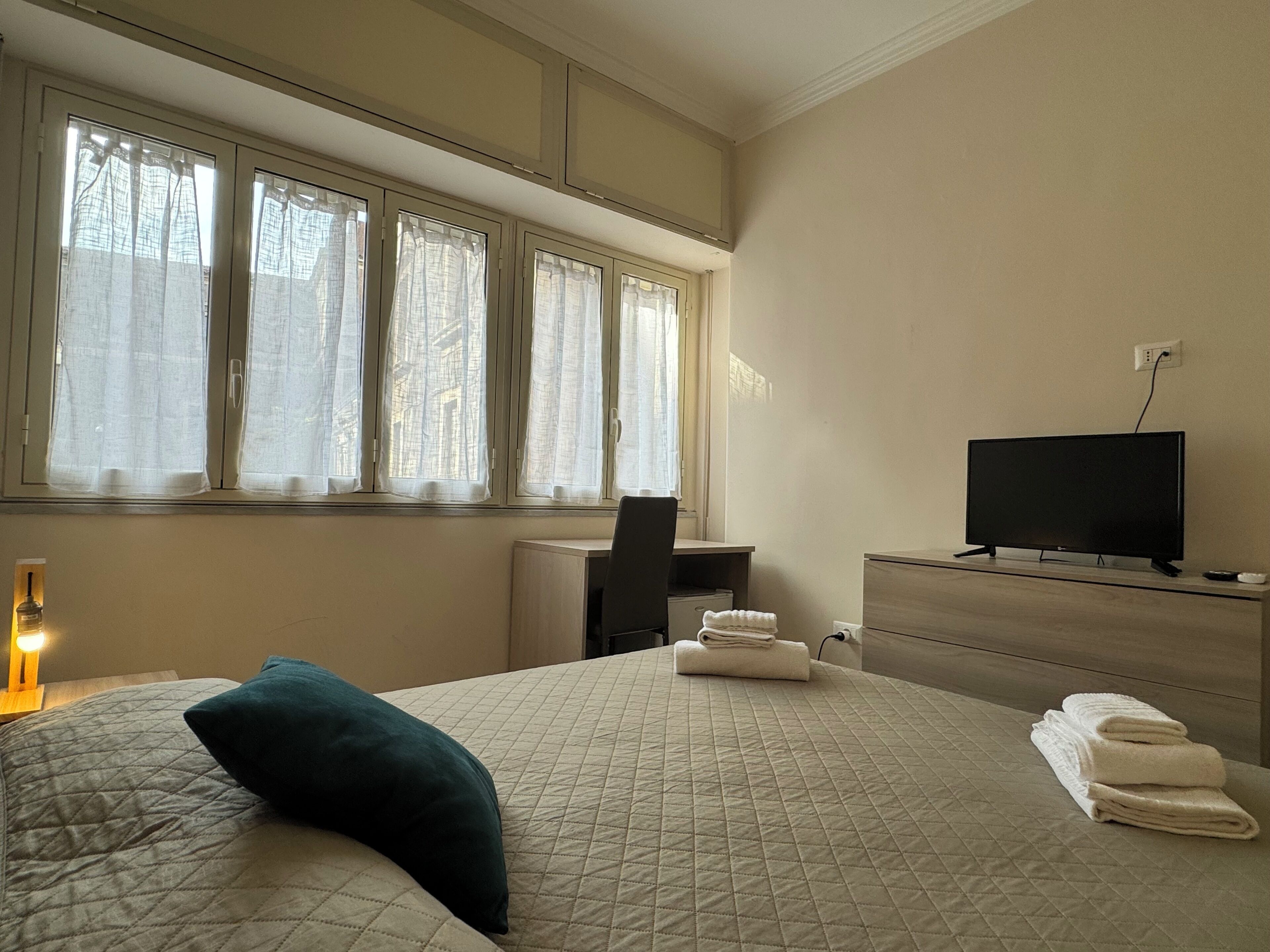 A hotel room with a bed, a desk, a television, and a window with curtains.
