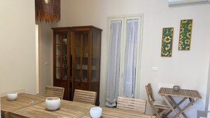 A dining area with a wooden table and chairs, a cabinet with glass doors, a small table with a bowl, and two curtains. - R&B Santa Nicolella (Catania)