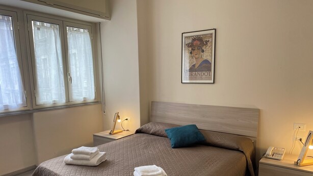 A neatly made bed with a quilted brown cover, two folded white towels, a blue pillow, and a framed picture on the wall. - R&B Santa Nicolella (Catania)