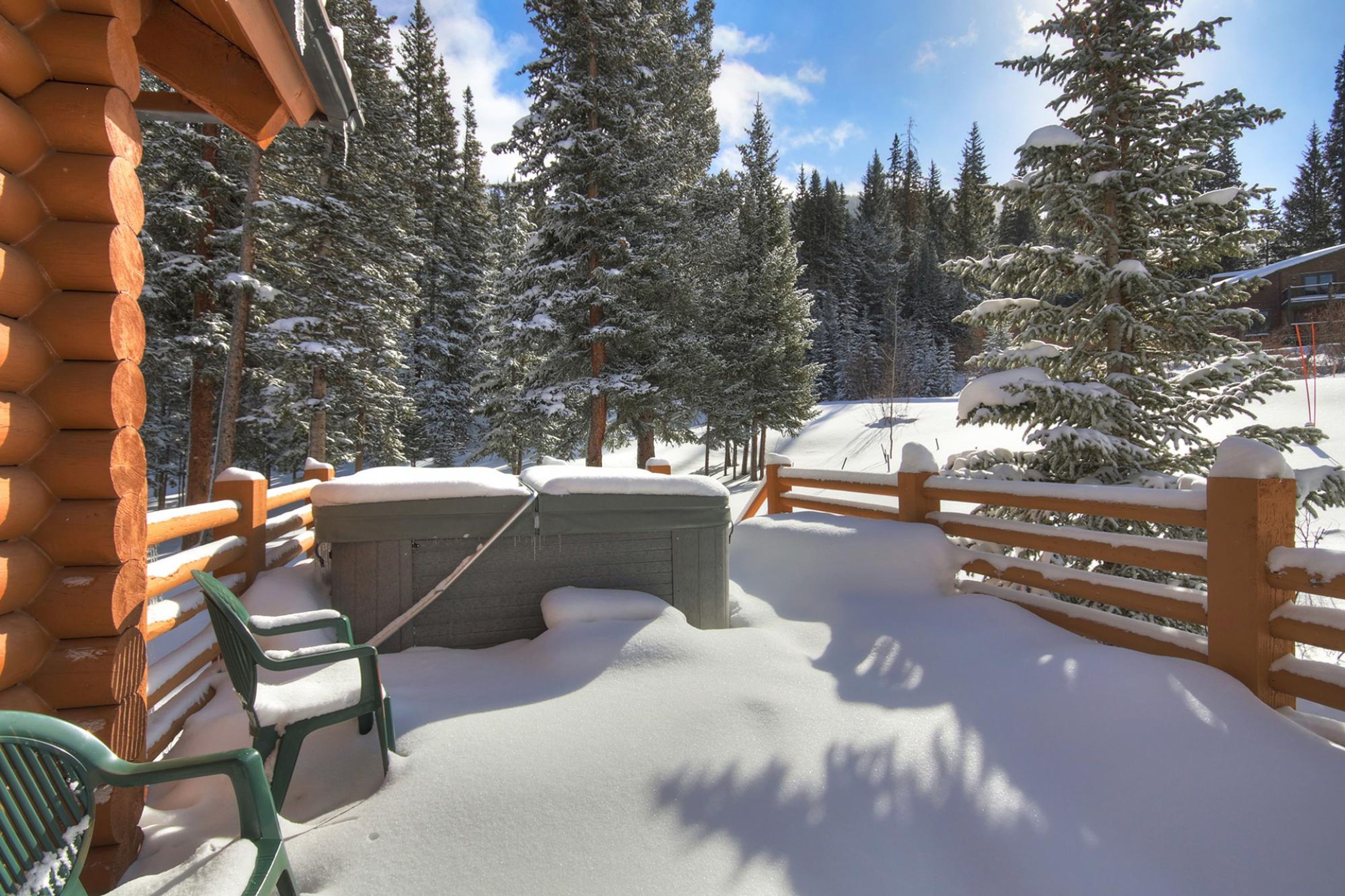 A wooden cabin with a snow-covered deck, a hot tub, and a wooden fence.