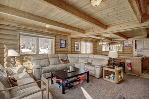 A log cabin interior with a sectional sofa, a coffee table, a small side table, and a kitchen area. - Cook Family Lodge in Breckenridge (Breckenridge)
